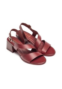 Sandalias de cuero rojo con correas cruzadas y hebilla ajustable en el tobillo, que cuentan con un tacón de madera cuadrado y un acabado suave.