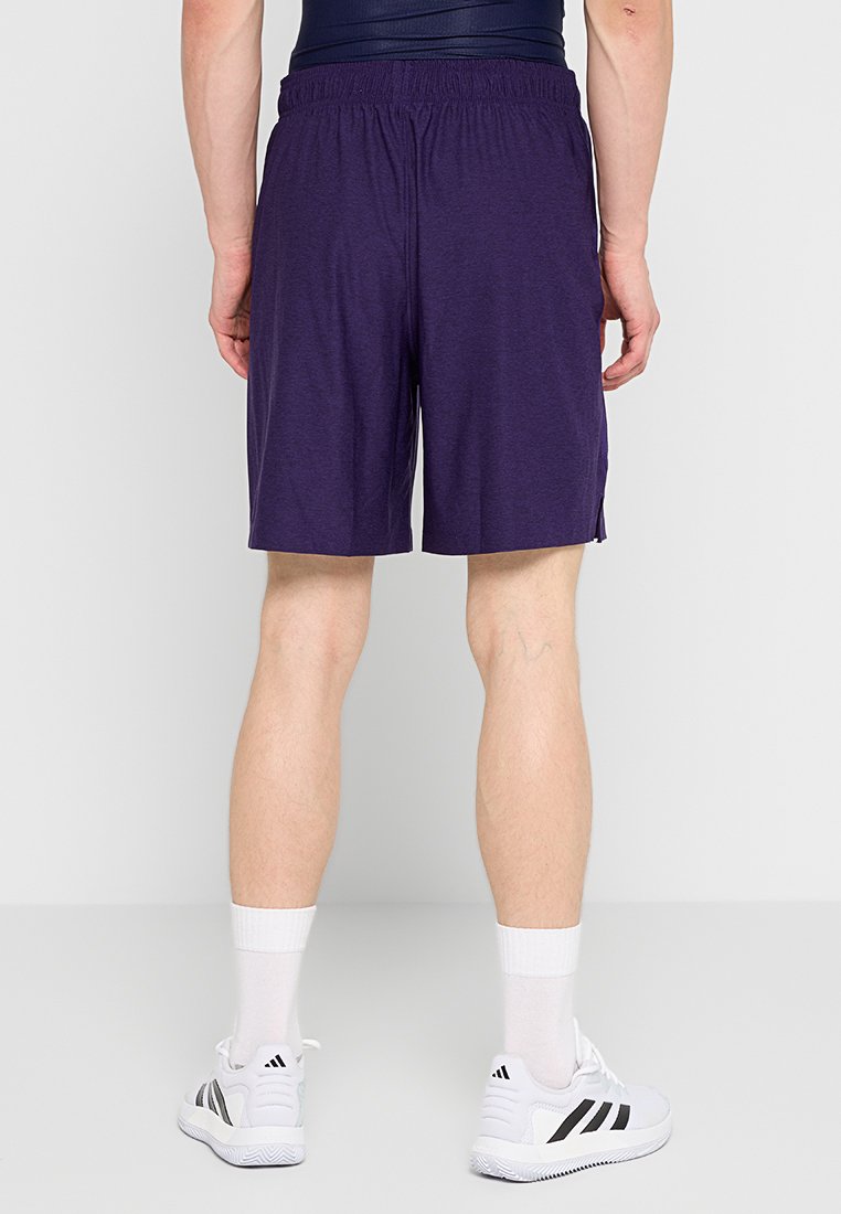 Pantaloni sportivi viola con cintura elastica, che arrivano a metà coscia. Indossati insieme a scarpe sportive bianche e nere e calzini di lunghezza a crew.