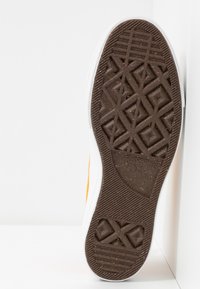 Semelle de chaussure avec motif de bande de roulement géométrique en caoutchouc marron, affichant le logo de la marque Converse et la taille 45 embossés près du talon.
