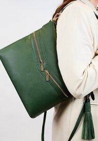 Groene lederen schoudertas met twee gouden ritsaccenten en een kwastdetail. Gladde textuur, rechthoekige vorm en verstelbare schouderband.
