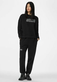 Czarny komplet bluzy i spodni z napisem "SOHO" i "IDHO" w kontrastowej bieli. Miękki materiał, luźny krój i ściągacze przy rękawach.