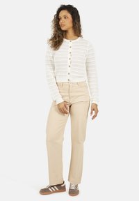 Biały sweter z dzianiny o teksturowanym wzorze i zapięciem na guziki, w zestawieniu z beżowymi spodniami prostymi i szarymi butami sportowymi z białymi paskami.