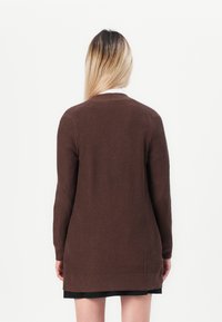 Brown ribbed cardigan with long sleeves, rounded neckline, and a straight cut, extending below the hips. Textured fabric visible.