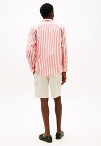 Chemise à manches longues rouge et blanche à rayures, faite d'un tissu léger, associée à un short cargo beige et des chaussures noires à enfiler.