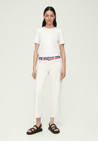 T-shirt blanc à manches courtes assorti à un pantalon blanc cropped, une ceinture multicolore avec des rayures bleues et rouges, et des sandales à lanières noires.