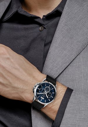 Chronograph Uhr mit blauem Zifferblatt, silbernem Gehäuse und schwarzem Lederarmband. Verfügt über drei Nebenzifferblätter und eine Datumsanzeige um 6 Uhr.