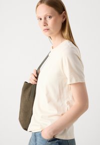 T-shirt crema a maniche corte con scollatura rotonda, abbinata a una borsa a spalla in tessuto verde. Design semplice, texture morbida, vestibilità casual.