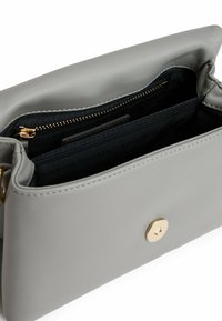 Bolso de cuero gris con un cierre de botón de presión dorado, desabrochado que revela un interior de tela oscura y compartimentos para la organización.