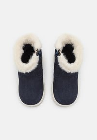 Bottines en suede bleu marine avec doublure en fausse fourrure blanche, fermetures éclair sur les côtés et semelles en caoutchouc clair. La vue du dessus révèle une texture lisse.