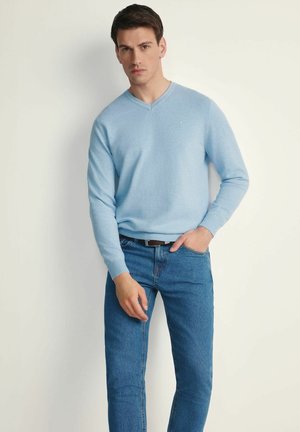 Jasnoniebieski sweter z dekoltem w serek wykonany z miękkiej dzianiny, w połączeniu z niebieskimi dżinsami. Sweter ma długie rękawy i dopasowaną sylwetkę.