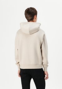 Beige Kapuzenpulli aus weichem Stoff, mit einer Kängurutasche und gerippten Bündchen. Rückansicht auf weißem Hintergrund.