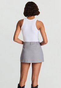 Weißes, geripptes Tanktop kombiniert mit einem grauen Minisrock, der eine taillierte Passform und eine glatte Textur aufweist. Schwarze kniehohe Stiefel sichtbar.