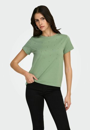 Grøn t-shirt i bomuld med dekorative sølvnitter fordelt i et spredt mønster. Korte ærmer og en afslappet pasform. Sorte jeans.