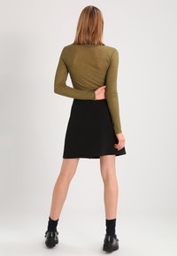 Top a maniche lunghe verde oliva abbinato a una gonna nera, caratterizzato da una texture liscia e una silhouette semplice. Scarpe nere con suola spessa.