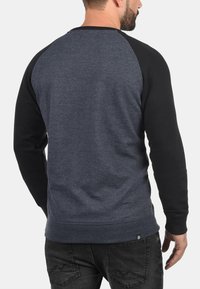 Pullover con maniche a raglan di colore blu scuro con maniche nere, realizzato in tessuto morbido. Presenta un collo rotondo e polsini a costine.