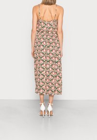 Woman standing facing away, wearing a sleeveless patterned midi dress with thin straps and white high-heeled sandals.