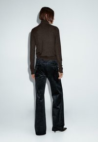Maglione a collo alto marrone abbinato a pantaloni a gamba larga in velluto a coste scuro. L'outfit presenta una finitura testurizzata e dettagli sottili in vita.