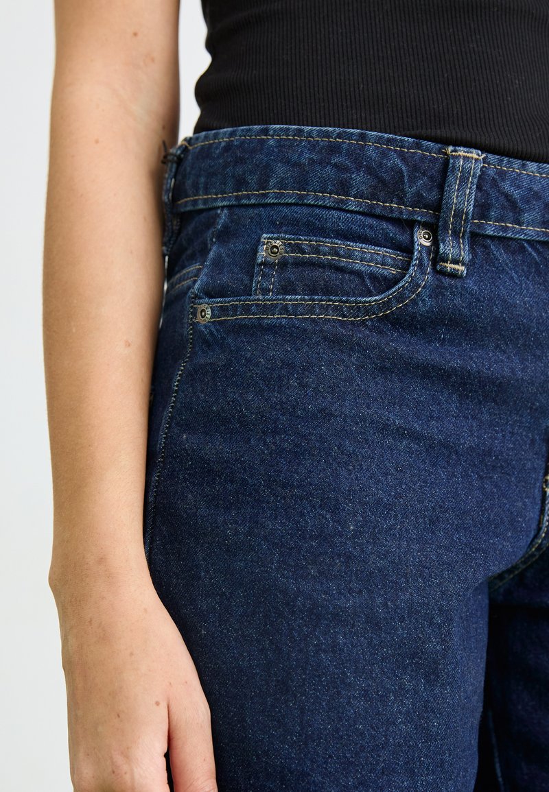 Jeans in denim blu scuro con un taglio classico. Caratteristiche includono tasche standard, cuciture visibili e una superficie liscia.