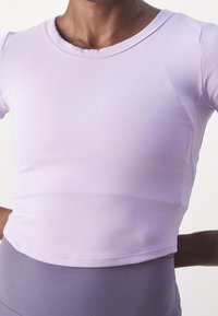 Close-up of person wearing a fitted light purple short-sleeve crop top and high-waisted lavender leggings against a white background.