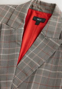 Grå og sort ternet blazer med rød satinfor, der har krave med hak og et mærke indeni mærket "NEXT".