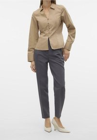 Beżowa dopasowana bluzka z długimi rękawami i zapięciem na guziki, w połączeniu z szarymi zwężanymi spodniami i kremowymi koturnami. Gładka faktura.