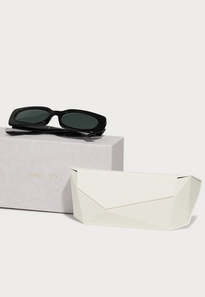 Crne prevelike sunčane naočale s tamnim staklima, u paru s bijelim geometrijskim tvrdom kutijom i svijetloružičastom kutijom s logom "JIMMY CHOO".