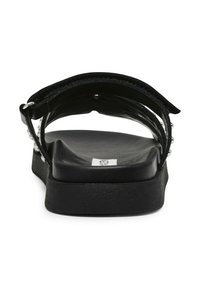 Des sandales noires plates dotées d'une semelle lisse, d'un dos ouvert et d'une sangle ornée d'accents argentés, présentant un design épuré et minimaliste.