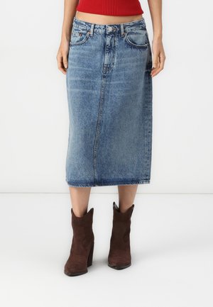 Denim midi-skjørt i lyseblått, med rett snitt, fem lommer, beltehemper og rå kant. Kombinert med brune skinnankelstøvler.