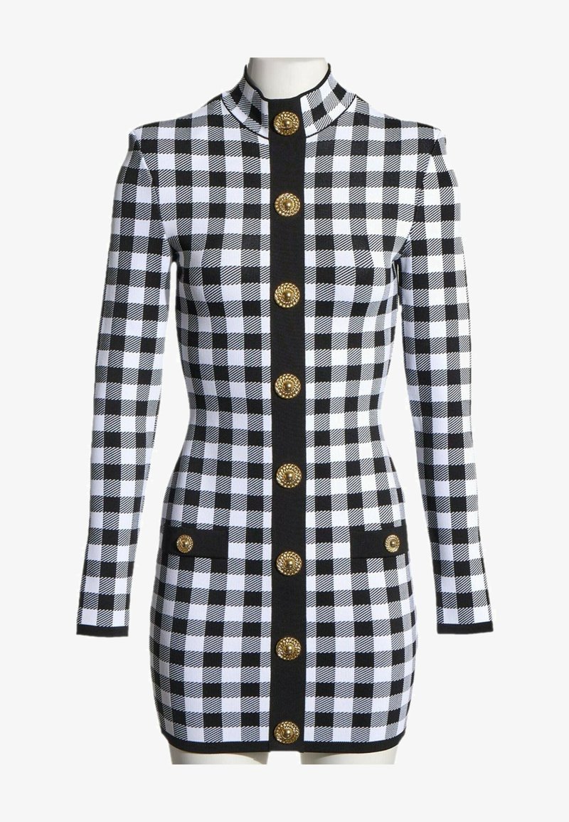 Robe à manches longues à carreaux noir et blanc avec un col montant, une bordure verticale noire et six boutons décoratifs dorés sur le devant et sur les poches.