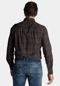 Donkerbruin geruit overhemd met gele en blauwe lijnen, lange mouwen, knoopmanchetten, gecombineerd met blauwe denim jeans en een geweven riem.