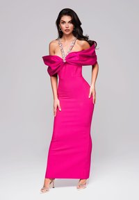 Fuksia off-the-shoulder mekko, jossa on dramaattinen solmuseidat, koristeltu kaulus ja vartalonmyötäinen siluetti, yhdistettynä kirkkaisiin, naruista tehtyihin korkokengiin.