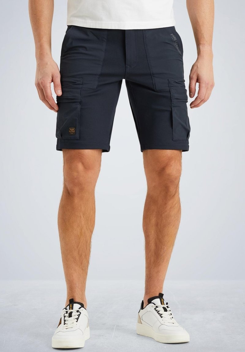 Marine cargoshorts met meerdere zijzakken, gemaakt van een gladde stof; gecombineerd met witte sneakers met zwarte accenten.
