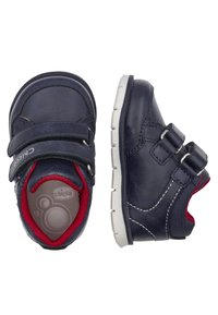 Chaussures pour tout-petits en cuir bleu marine avec double bande Velcro, semelle en caoutchouc blanche, doublure rouge et détails de coutures blanches. Design à bout rond.