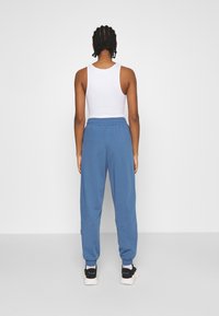 Blå bomullsjoggers med smal benända, elastisk midja och kontrasterande sidostrick, i kombination med en tajt vit topp.