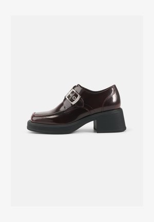 Scarpe in pelle verniciata bordeaux con punta quadrata, tacco a blocco e dettaglio con fibbia laterale. Presentano una finitura liscia e una morbida consistenza.