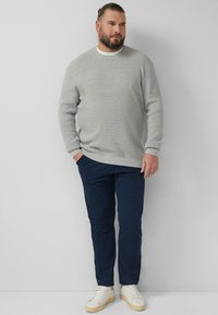 Pull en tricot gris, pantalon bleu marine et baskets blanches. Le pull présente un col rond et des manches longues. Design simple et moderne.