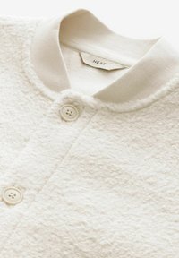 White textured fleece jacket with a contrasting light grey collar, featuring two cream buttons and a label reading "NEXT."