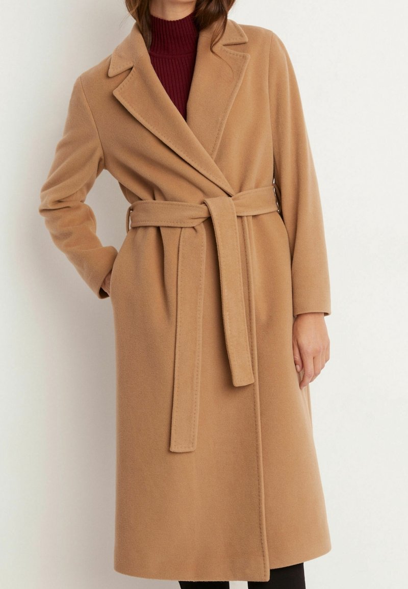 Beige omslagsrock i mjukt material, med bälte i midjan, slagkrage och långa ärmar, i kombination med en bordeauxfärgad polotröja.