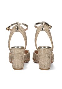 Las sandalias de tacón alto doradas con tiras tienen una textura decorada con cuentas, un tacón grueso y una correa ajustable en el tobillo con un detalle de hebilla metálica.