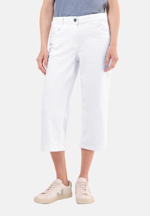 Witte cropped broeken van katoenmix, met een knoopsluiting en twee voorzakken, in combinatie met lichtgekleurde sneakers.