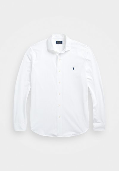 Baltā garo piedurkņu pogām aizdaram kocie krekls. Iezīmē klasisko apkakli, regulāru piegriezumu un mazu tumši zilu logotipu krūšu daļā.