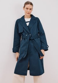 Marineblauer Trenchcoat mit tailliertem Gürtel, Reverskragen und Knopfdetails. Verfügt über einen seitlichen Schlitz und lange Ärmel mit geknöpften Manschetten.