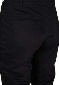 Pantalones de mezclilla negros con una textura suave, corte ajustado, dos bolsillos traseros con detalles de costura y una cinturilla clásica.