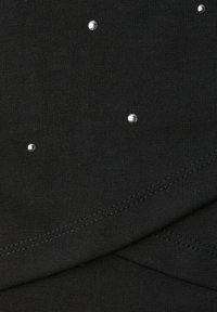 Czarna tkanina o gładkiej fakturze, ozdobiona rozmieszczonymi srebrnymi ćwiekami. Prosty wzór z płaskimi szwami, bez dodatkowych wzorów.