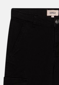 Schwarze Jeanshose mit Knopfverschluss, Gürtelschlaufen und Fronttaschen. Glatte Textur mit sichtbaren Nahtdetails.
