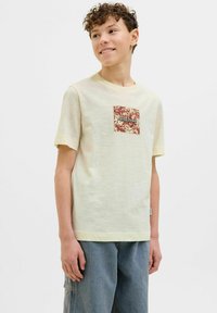 Šviesiai geltona medvilninė marškinėliai su kvadratiniu raudonu gėlių aplikacija ir tekstu "Jack&Jones." Trumpomis rankovėmis ir laisvu siluetu.