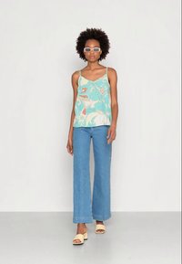 Camisola de alças finas em azul clara com padrão, combinada com jeans fluídos de cintura alta em azul clara e mules bejes de bico aberto.