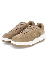 Beige Wildledersneaker mit perforierter Spitze, flachen Schnürsenkeln, gepolstertem Schaft und weißer Zwischensohle. Mit einem Markenlogo an der Seite.