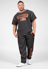 Donkergrijze outfit met oranje accenten. Ruimvallend T-shirt met het "GORILLA WEAR" logo. Bijpassende broek met zijstrepen en logo-detail.