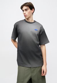 Γκρι μπλουζάκι με διαβάθμιση χρώματος και στρογγυλή λαιμόκοψη. Διαθέτει μικρό μπλε λογότυπο στο στήθος. Το ύφασμα φαίνεται μαλακό με άνετη εφαρμογή.